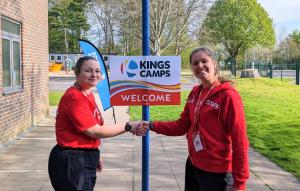 Two coaches shaking hands in front of a Kings Camps sign